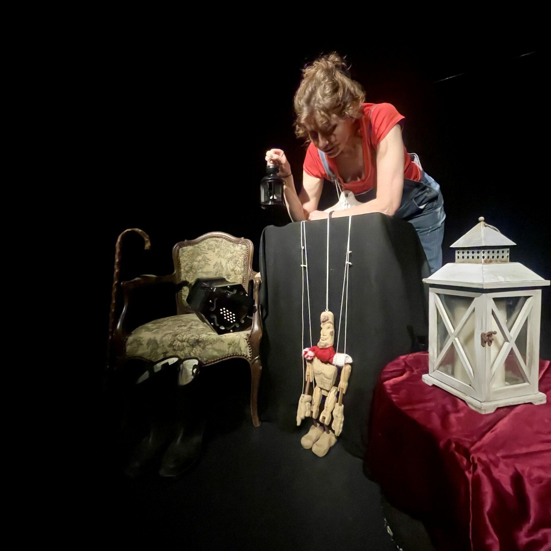 une marionnettiste sur un fond noir avec un fauteuil, une lanterne orientale poée sur une table