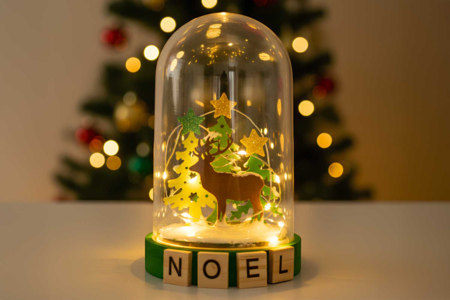 cloche en verre avec un renne en bois à l'intérieur, illuminée par une guirlande